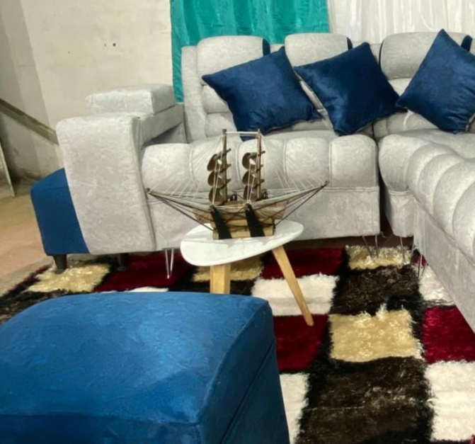 Sofá seccional azul y gris con almohadas, otomana y decoración de velero sobre una alfombra a cuadros.