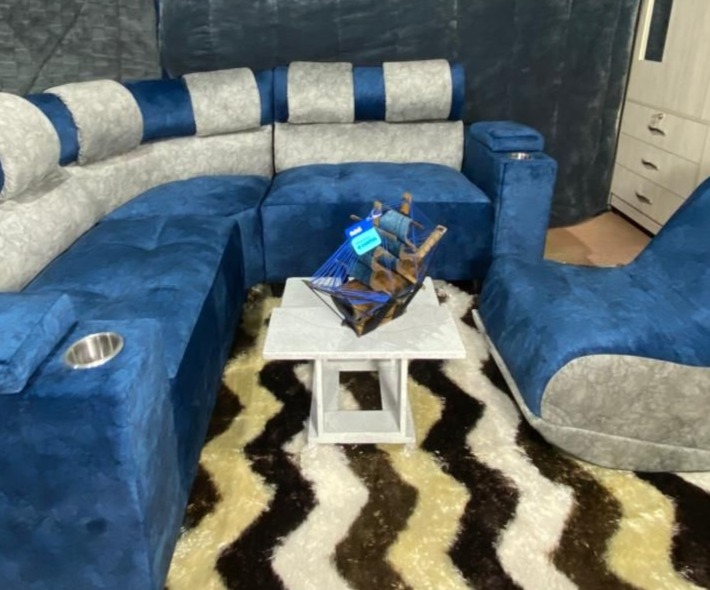 Sofá seccional azul y gris con una mesa cuadrada blanca y una alfombra estampada en una habitación.