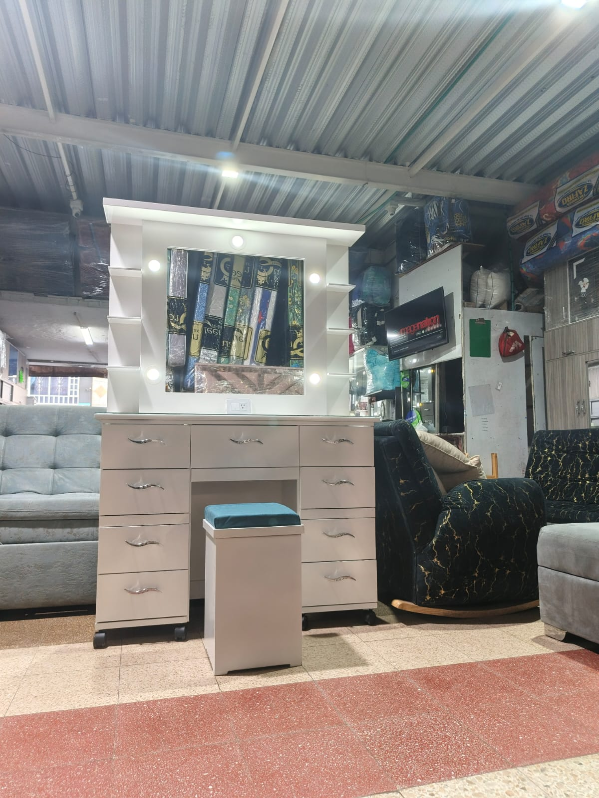 Tocador blanco con espejo, luces, cajones y taburete. Expuesto en una tienda.