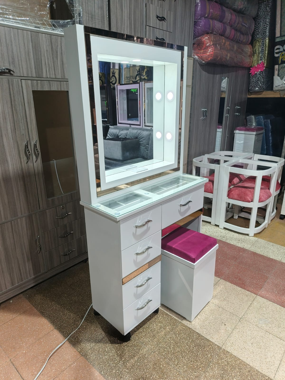 Tocador blanco con espejo iluminado, cajones y taburete, en una tienda de muebles.