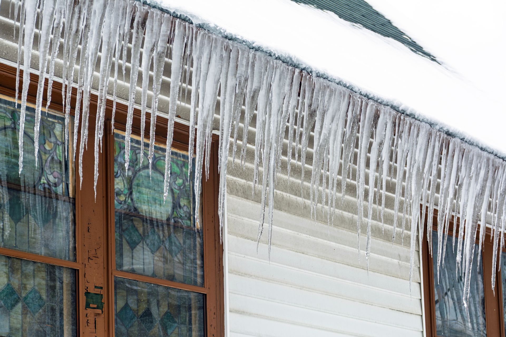 Large icicles hanging from a snow covered roof edge above exterior windows. Large icicles hanging from a snow covered roof edge above exterior windows.
