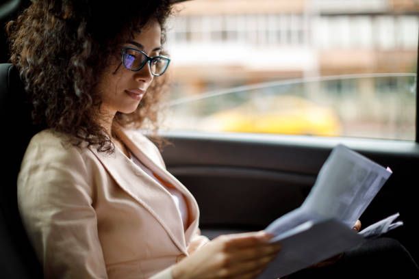 A woman is sitting in the back seat of a car reading a piece of paper.