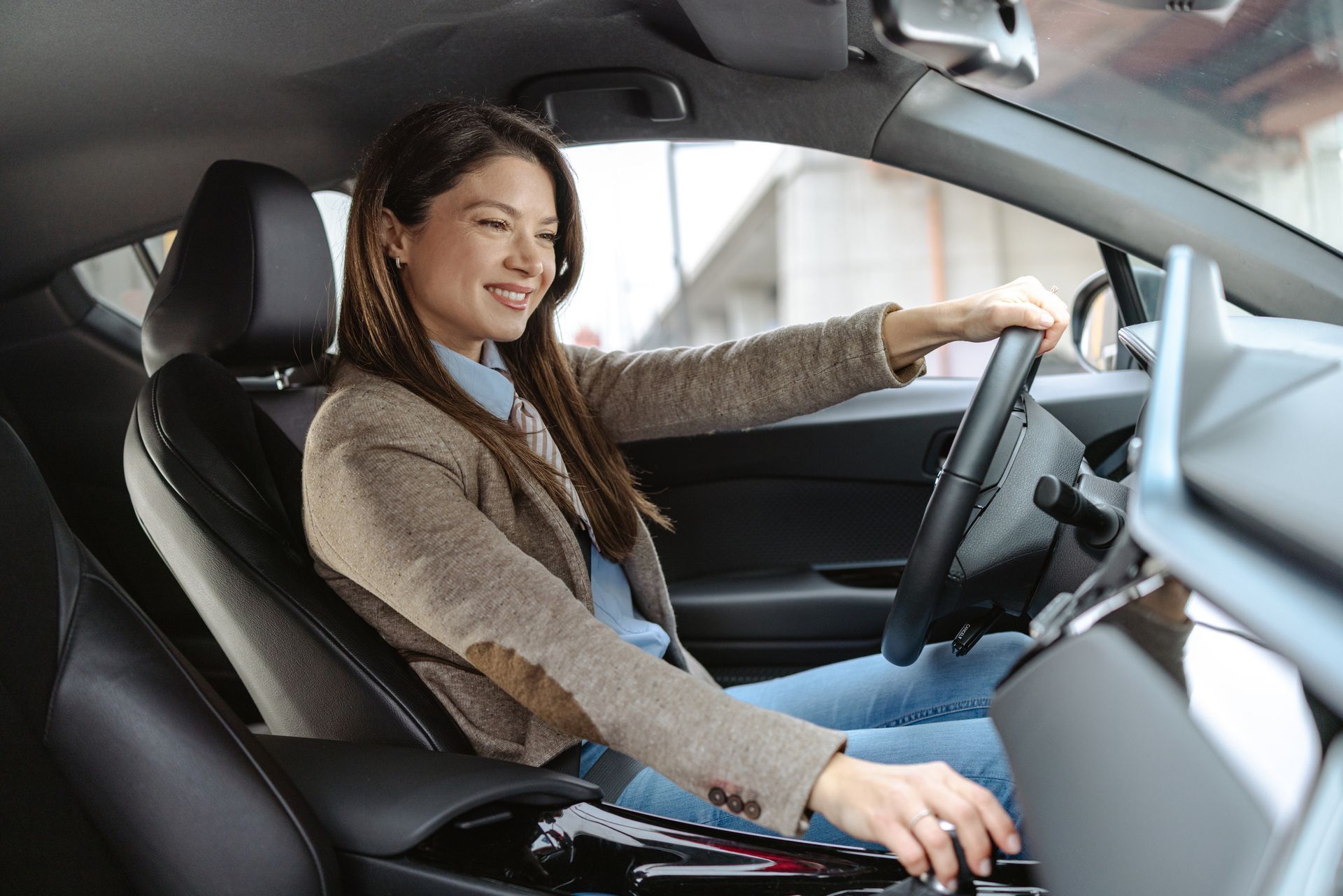 Smiling elegant woman confidently driving a car, showcasing the importance of auto insurance.