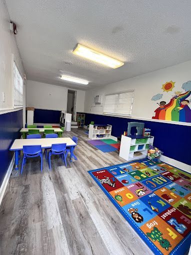 A classroom with tables and chairs and a rug on the floor.