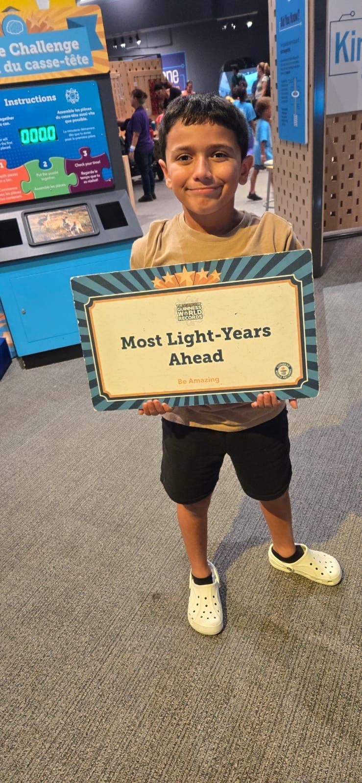 Exterior of a light yellow building with brick columns. Entrance has a sign, door, and potted plants. Lush green trees are in the background.
