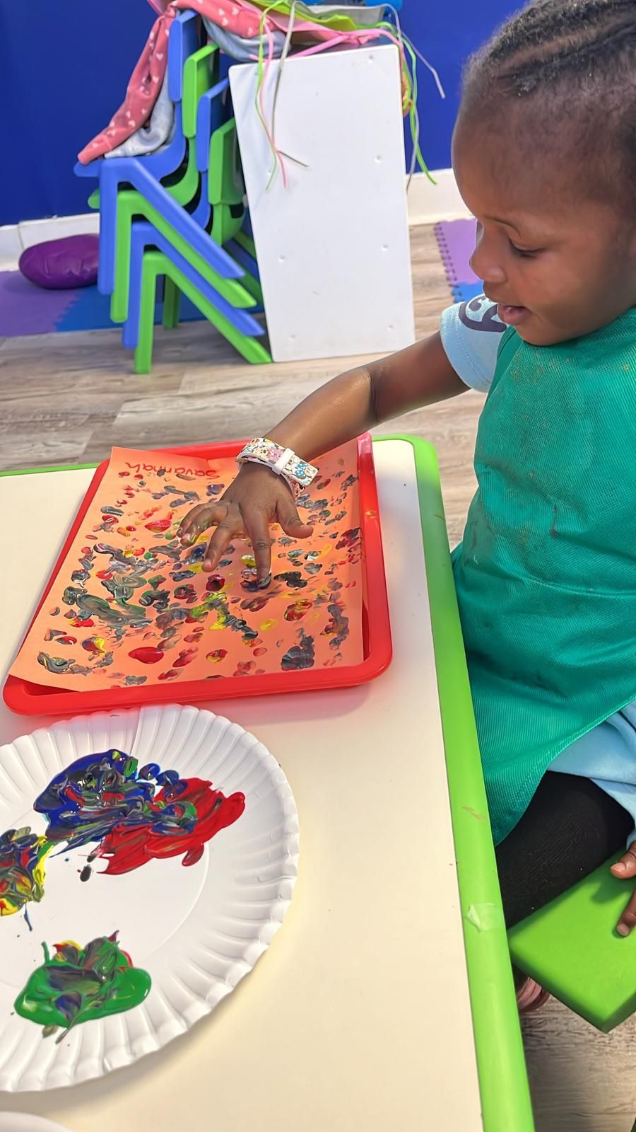 Young child painting with colorful paints, indoors, smiling.