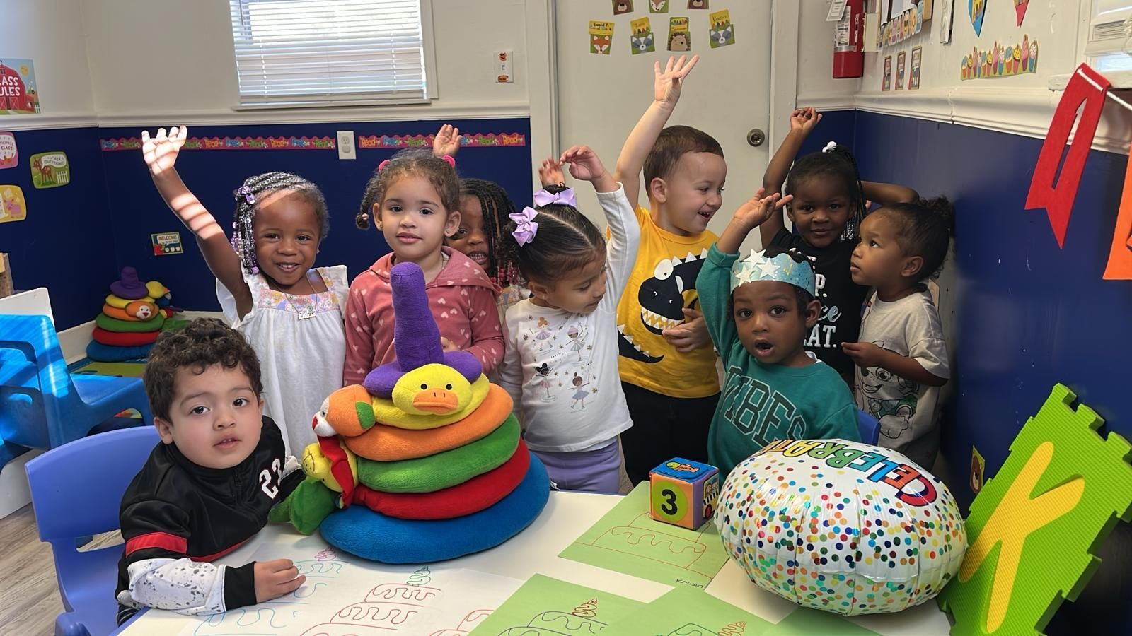 Brightly lit, colorful preschool classroom with tables, toys, and learning stations.