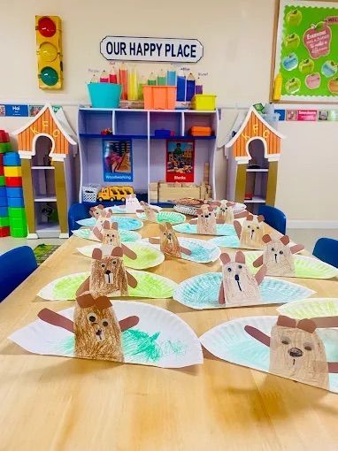 Crafts on a table in a classroom. Paper plate animal figures, with brown and green accents, sit on a wooden table.