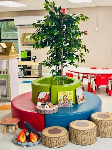 Playroom with tree, colorful seating, toy campfire, log stools, and books.