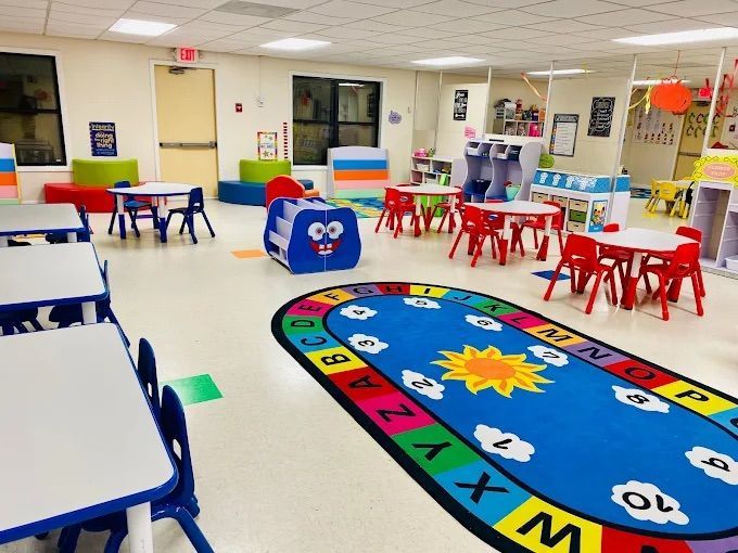 Classroom interior with tables, chairs, colorful rug, and play area.