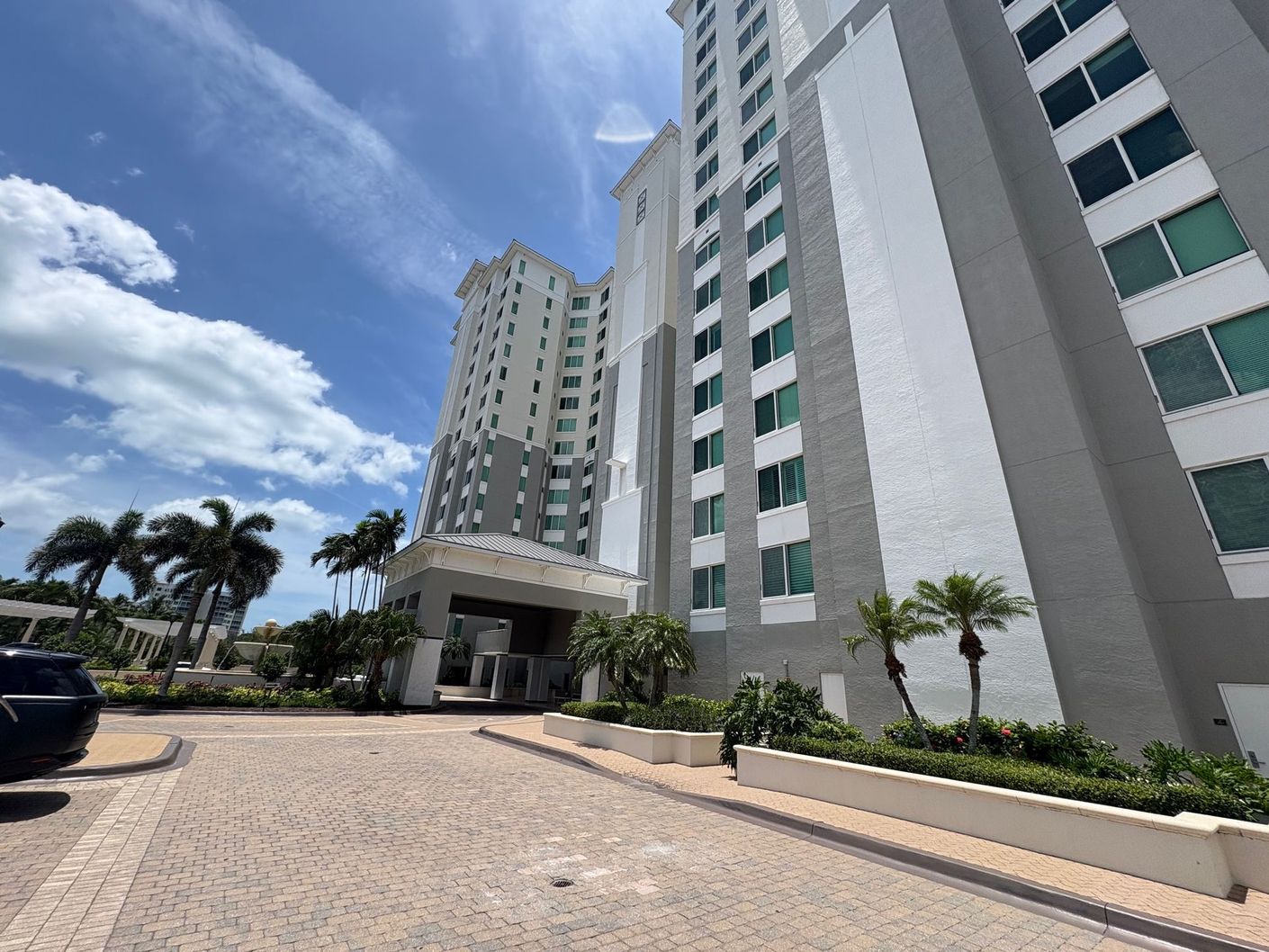 Tall gray and white hotel building with palm trees under a bright blue sky.
