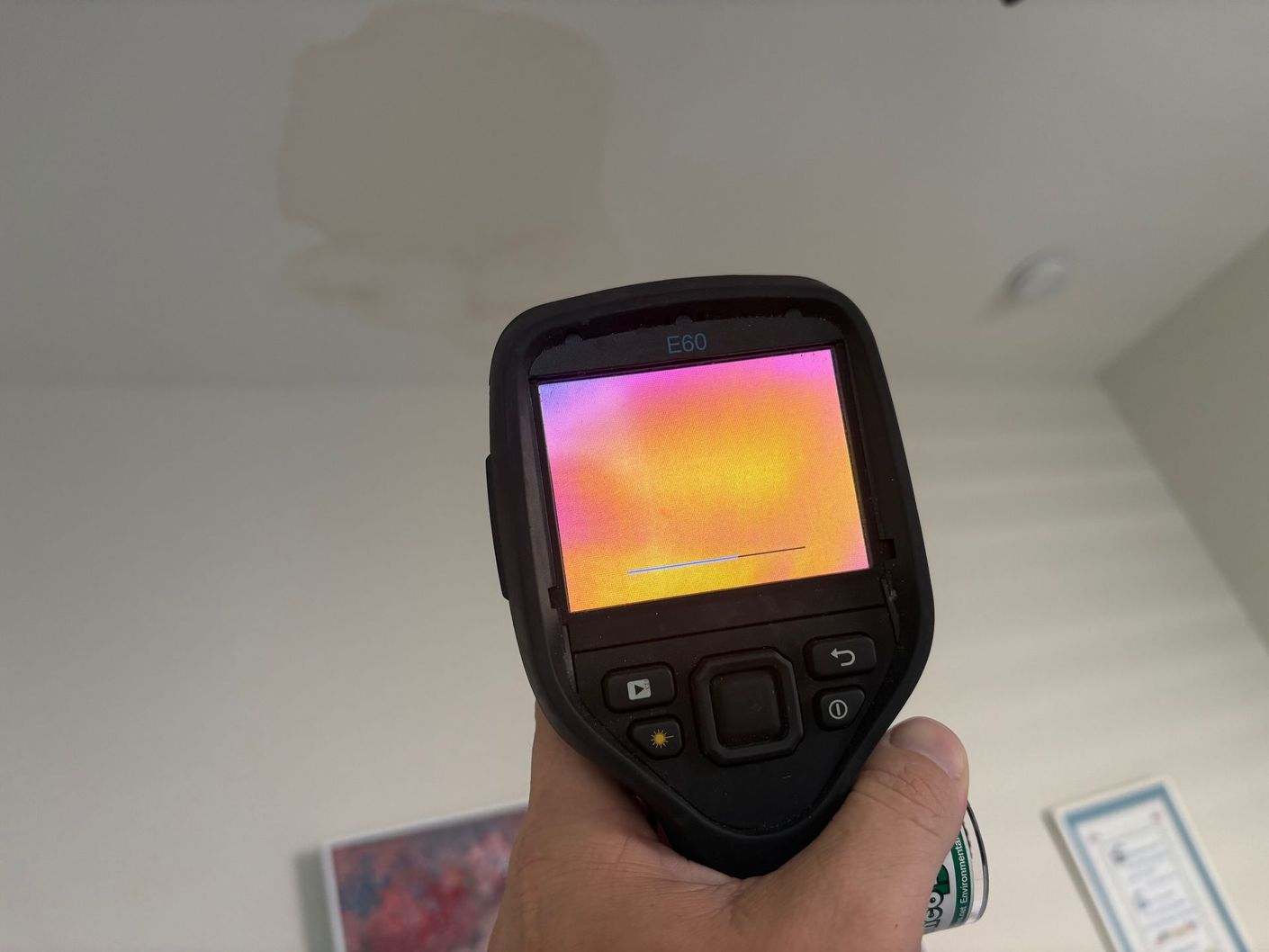 Hand holding thermal camera, showing heat map of ceiling with suspected water damage.