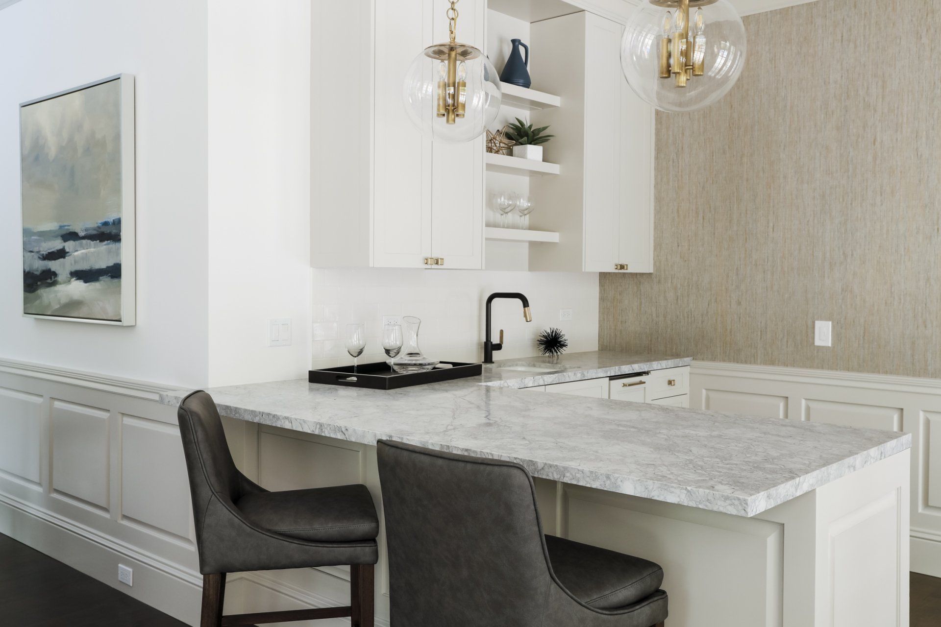 Supple Homes project in Atherton California. L-shaped wet bar with white cabinets and white countertops and gray leather bar stools. Two light pendants with gold hanging from the ceiling over the bar.
