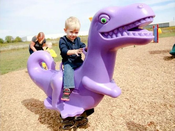 Boy on purple dinosaur spring toy at playground.