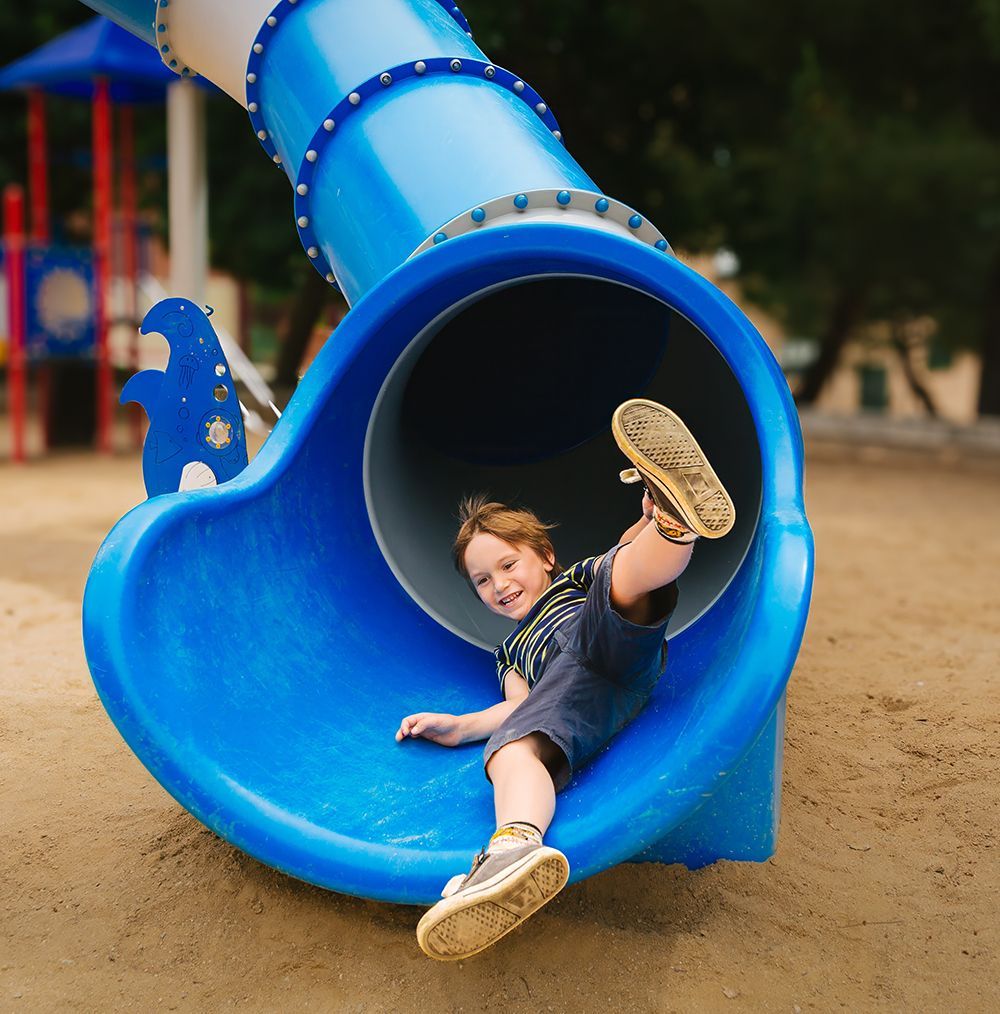 Boy sliding down blue playground tube, smiling.