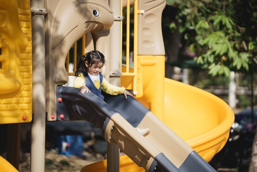 Child slides down a yellow and blue playground slide outdoors.