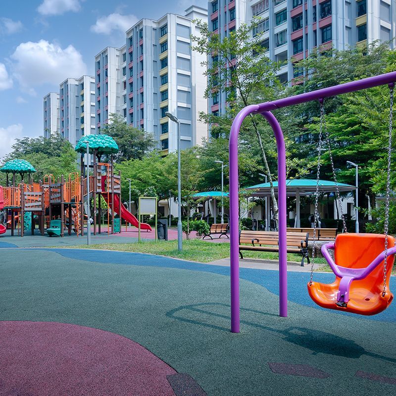 Playground with swings and slides, in front of high-rise apartment buildings.
