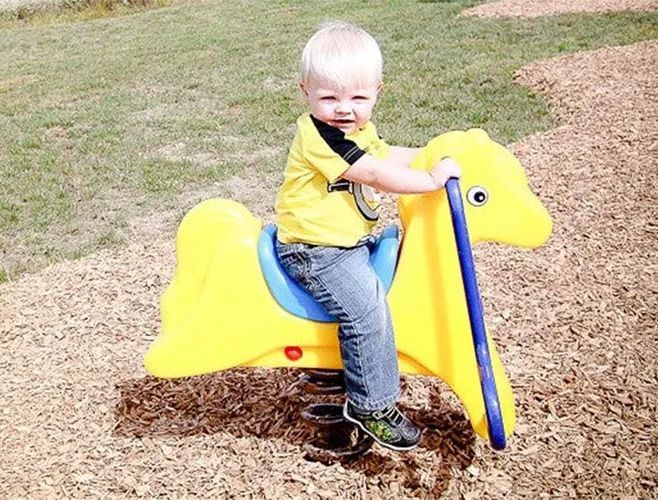 Blond toddler on a yellow and blue spring-mounted horse on a wood-chip playground.