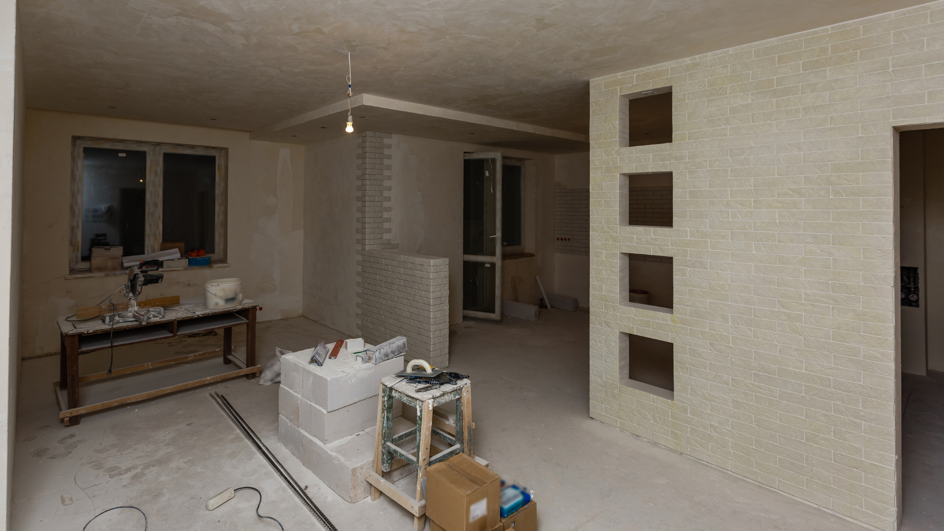 Interior room under construction, with exposed walls, windows, and construction materials.