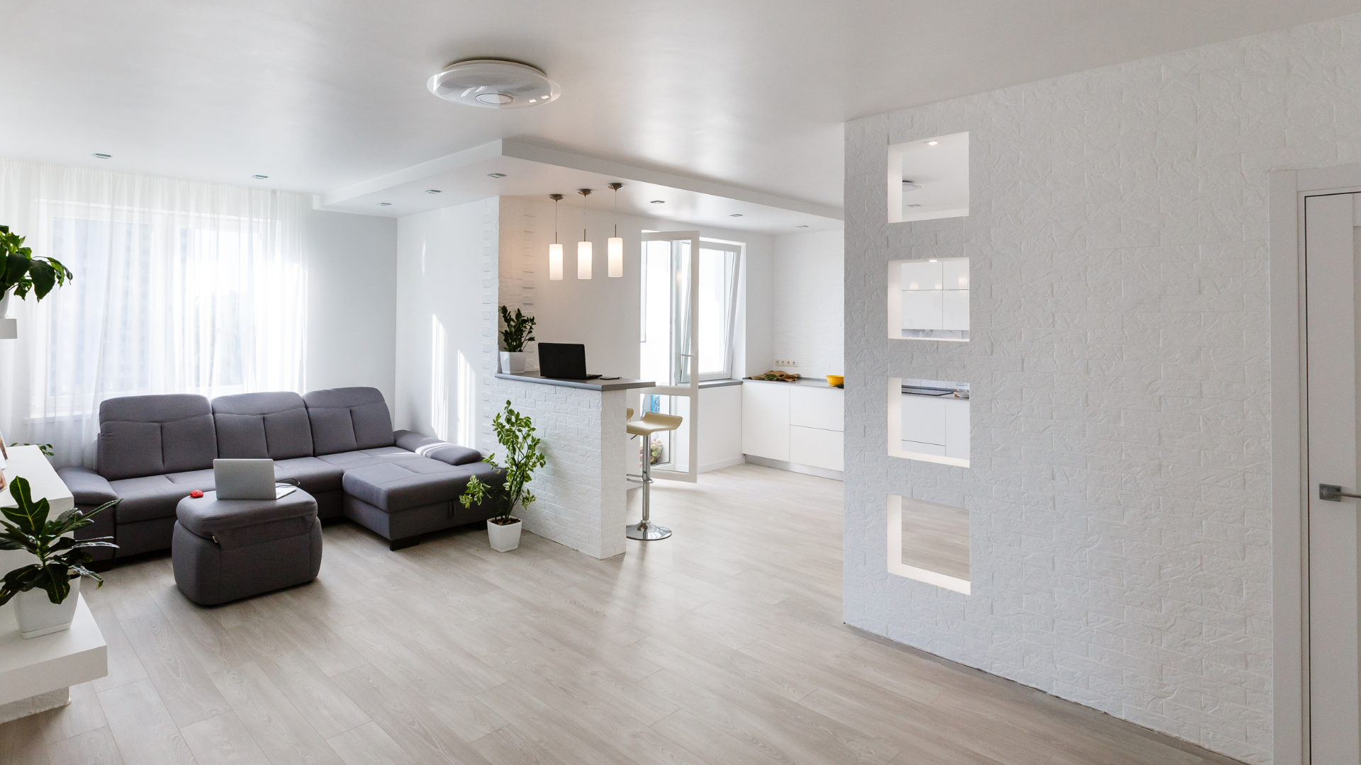 Modern, bright living space with gray sectional sofa, light wood floors, and white walls.