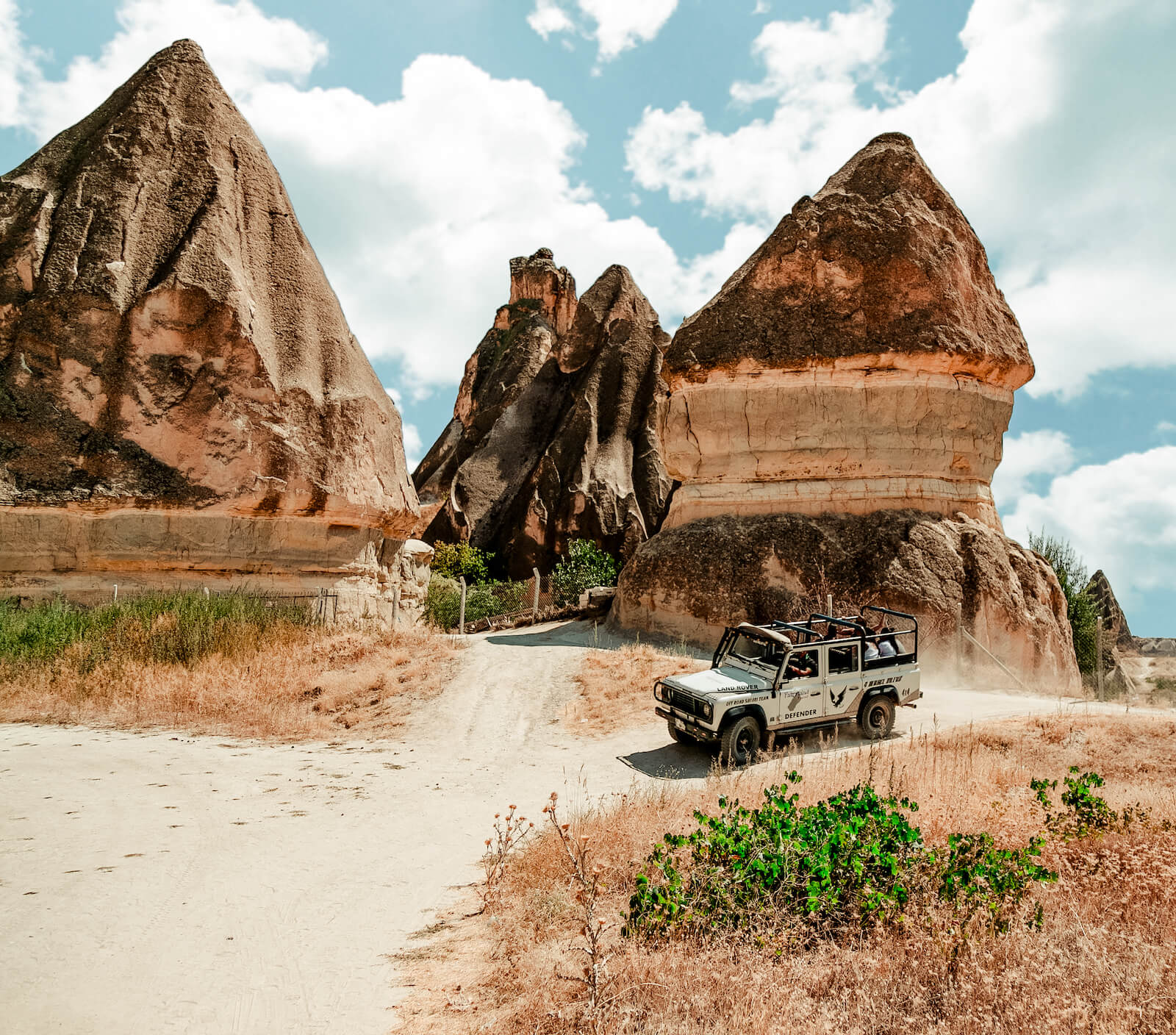A white jeep is driving down a dirt road in front of rock formations.