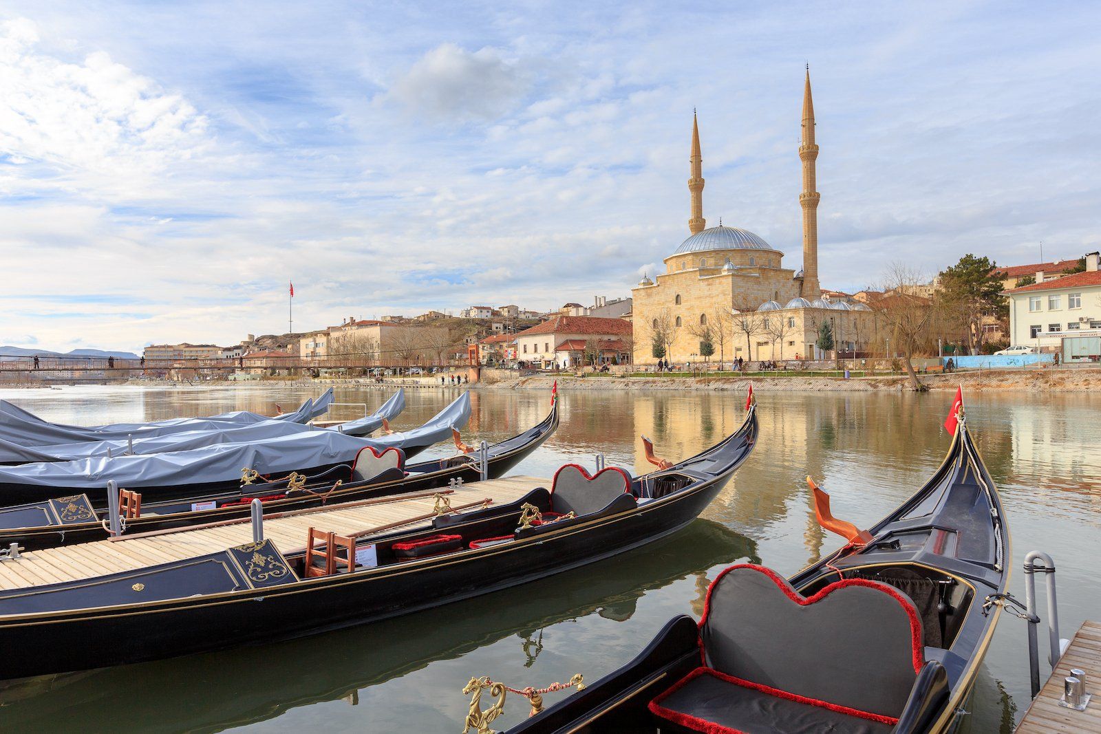 A row of gondolas are docked in a lake with a mosque in the background.