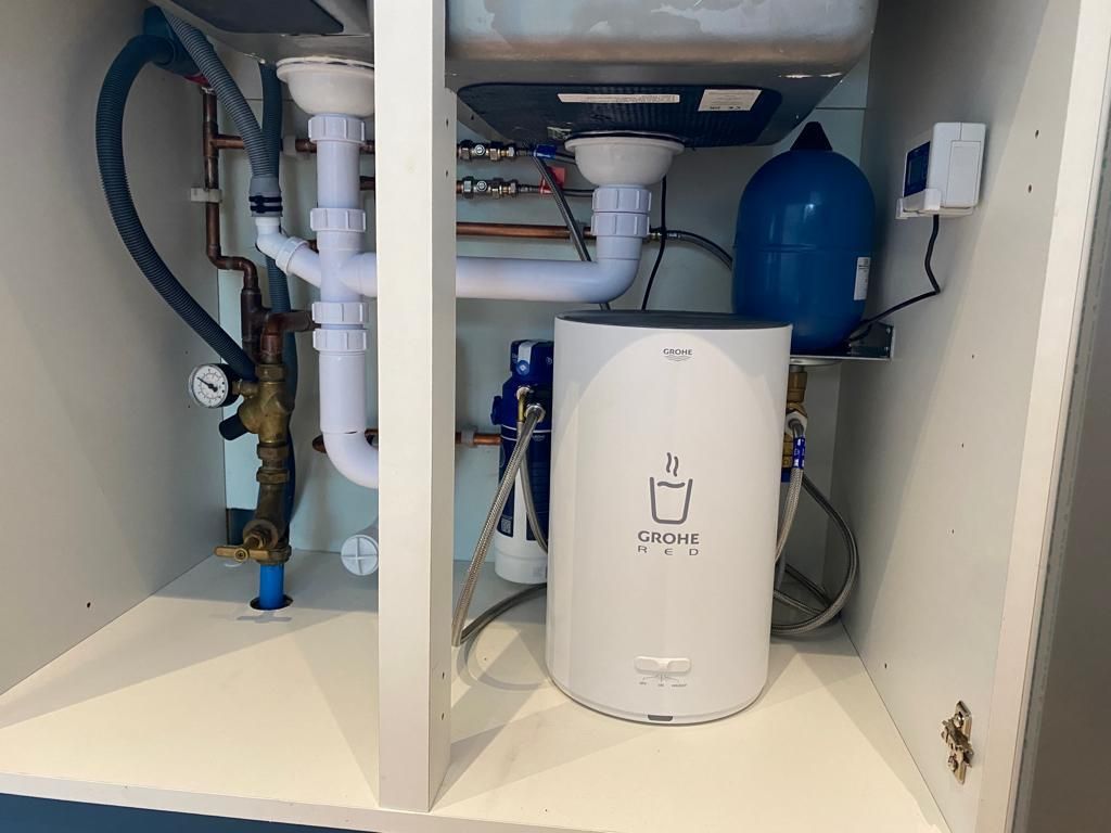 A white water heater is sitting under a sink in a cabinet.