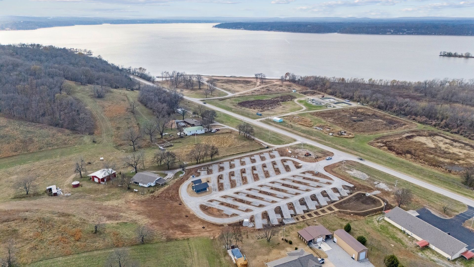 Aerial view of a parking lot for a boat launch area near a large body of water surrounded by grassy hills and trees.