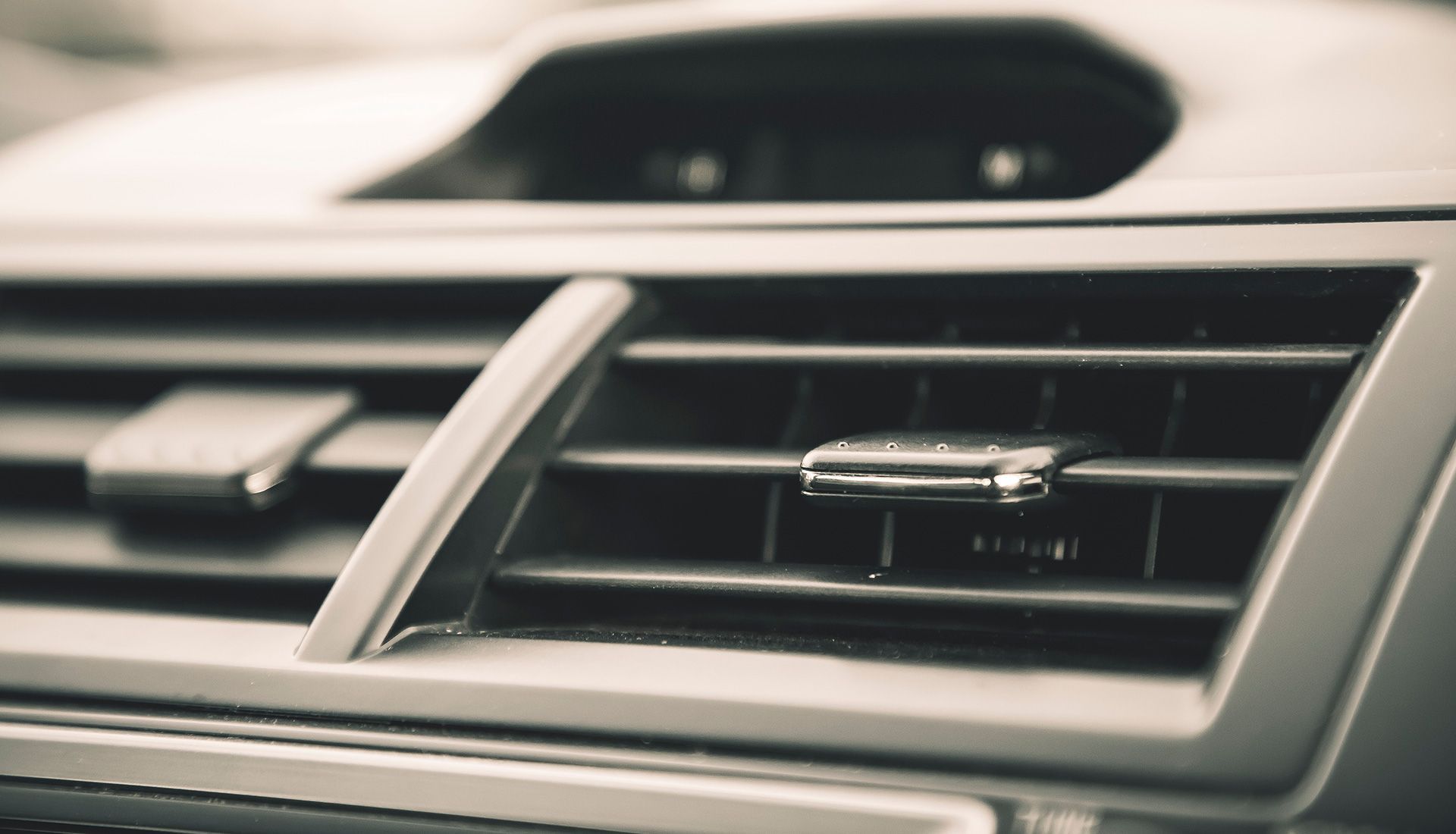 Close-up of a car's air vent, featuring horizontal slats and a silver control tab.