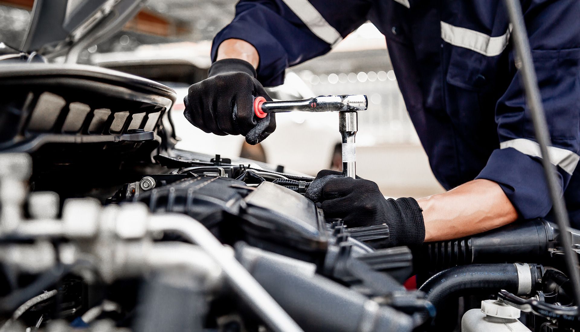 Mechanic in blue uniform working on a car engine with a wrench.