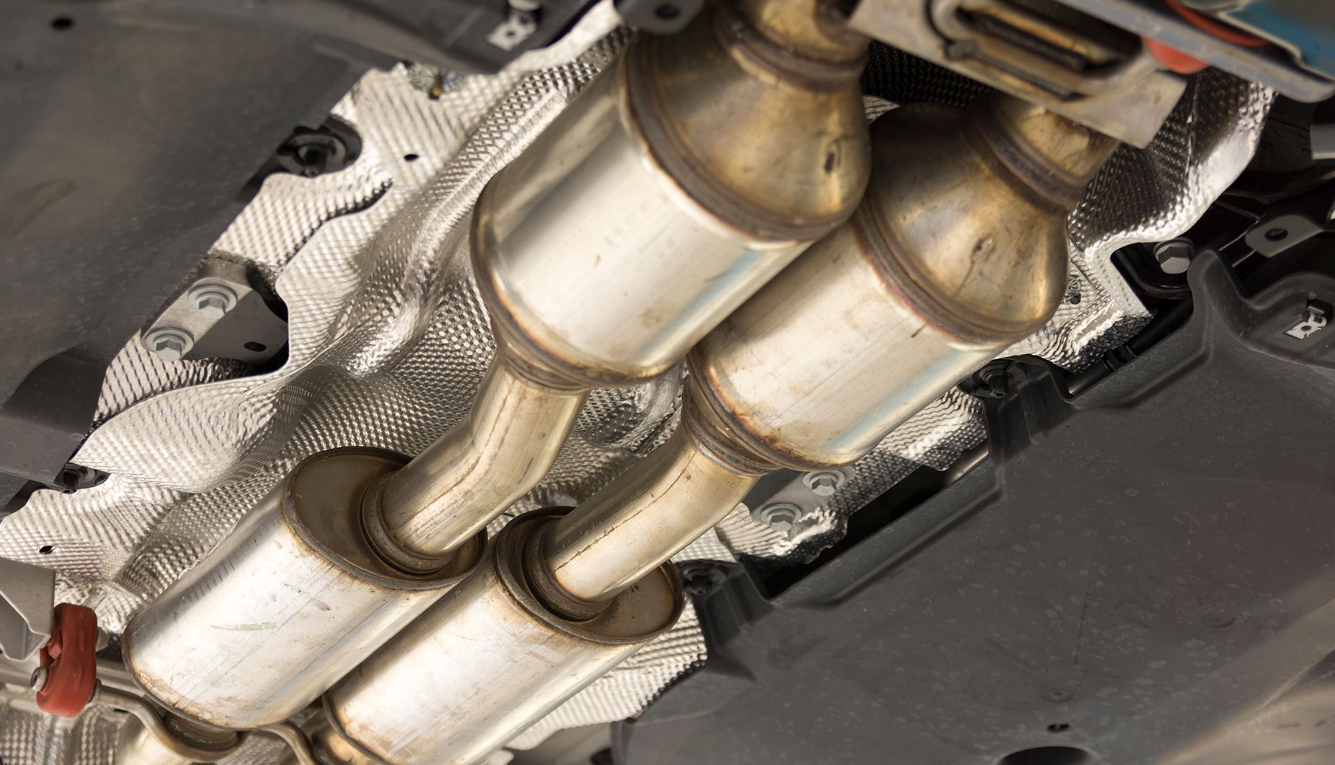 Underside of a car showing two catalytic converters, attached to exhaust pipes, with heat shields.