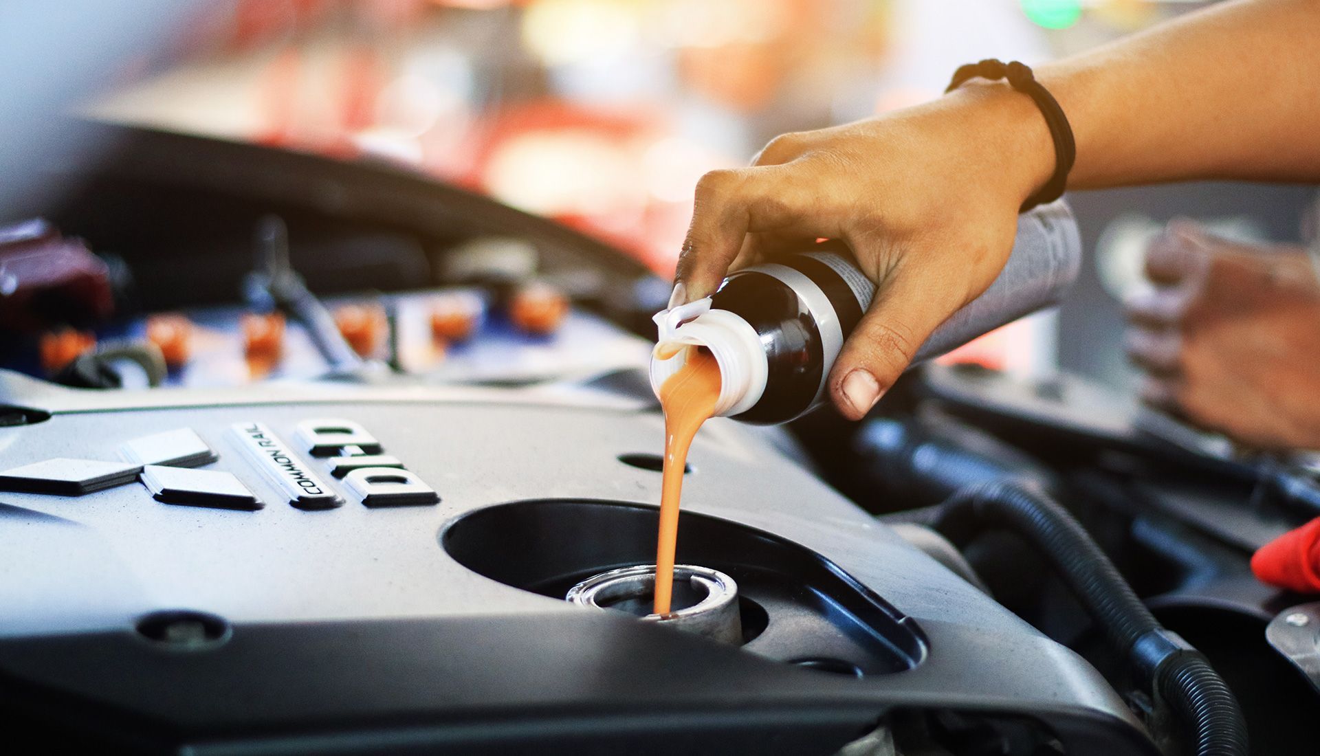 Hand pouring oil into a car engine.