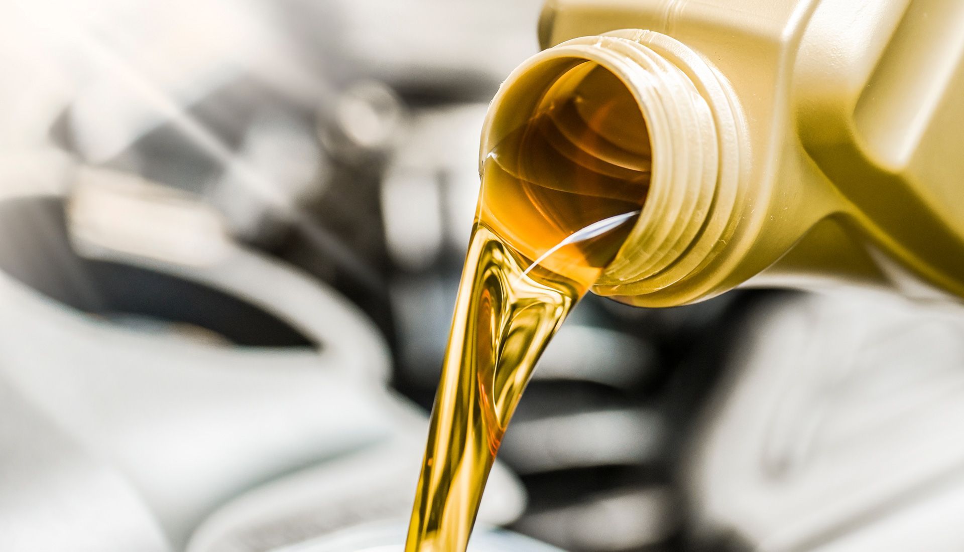Yellow motor oil pouring from a container into a car engine.