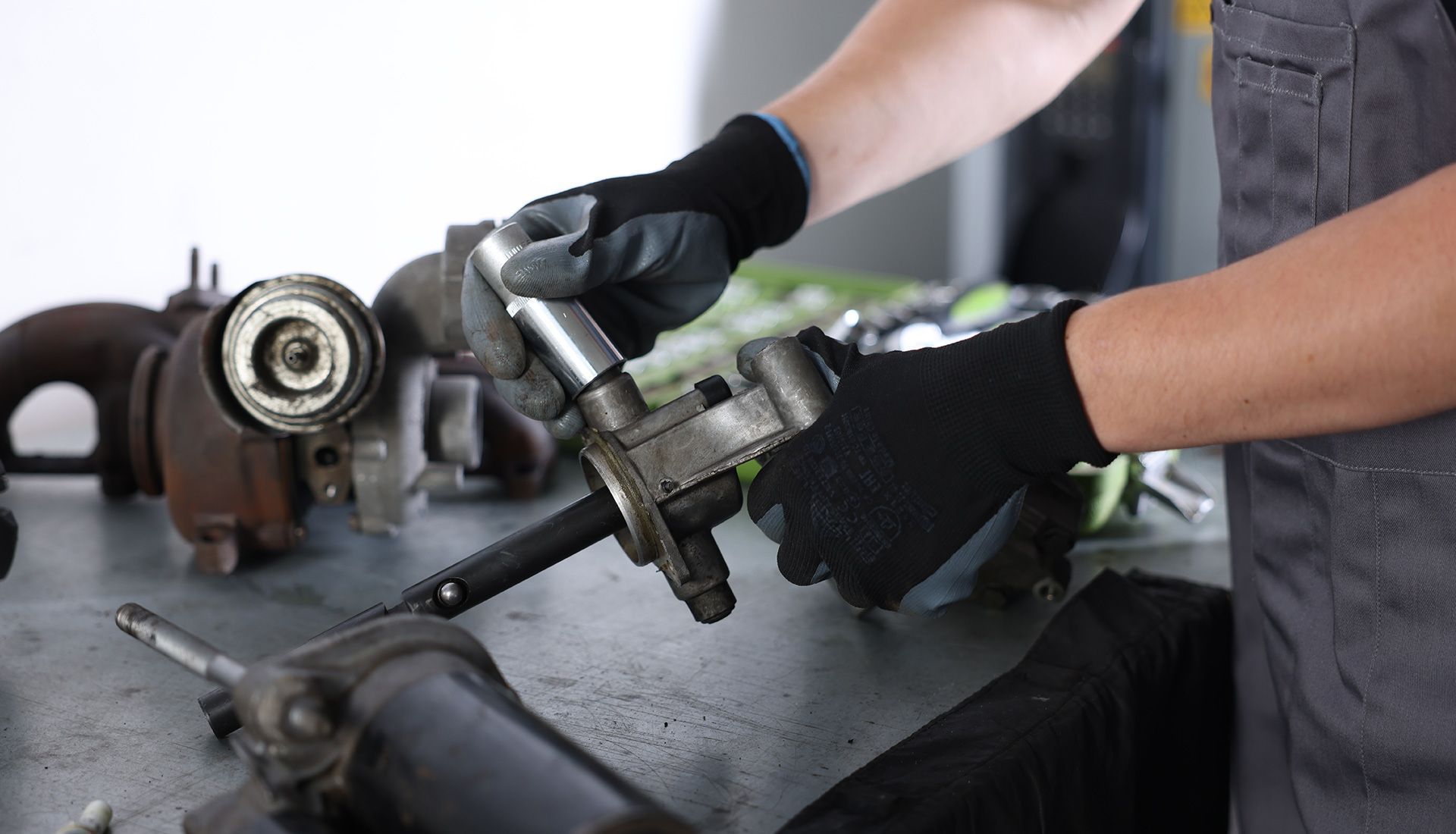 Mechanic with black gloves working on car parts at a table.