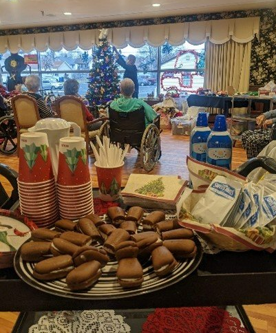 Seniors in a decorated room watching someone put a star on a Christmas tree. A table of treats is set up.
