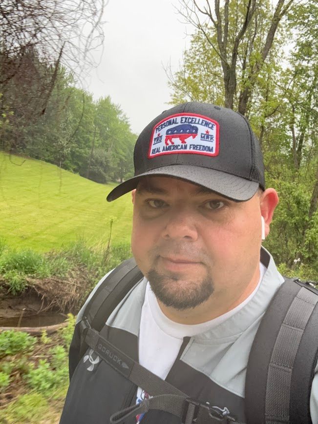 Jeff wearing a hat and backpack on a grassy path.