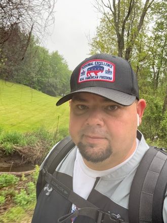 Jeff wearing a hat and backpack on a grassy path.