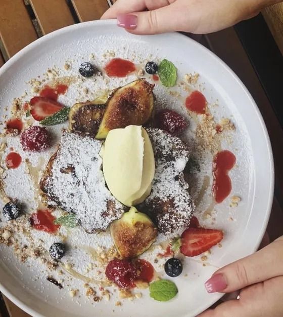 A person is holding a plate of food with berries and powdered sugar