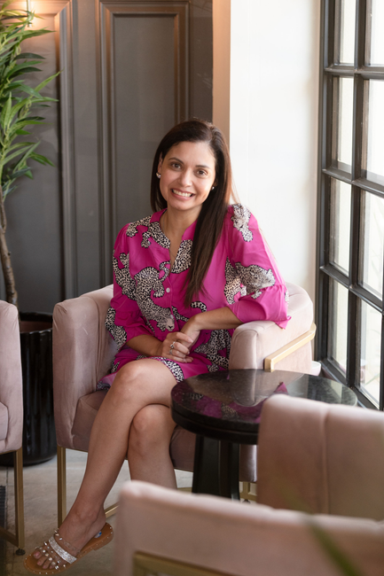 A woman in a suit is sitting on a wall and smiling.