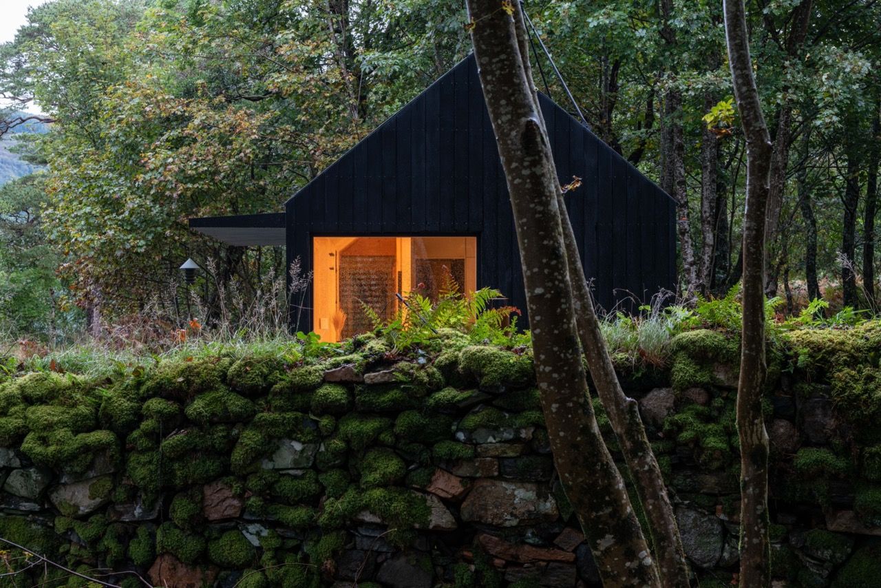 Black modern cabin behind an ancient stone wall.
