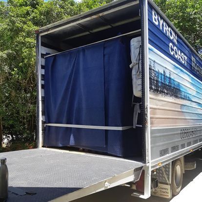 A Truck Has The Back Open With A Blue Curtain — Byron Coast Removals In Main Arm, NSW