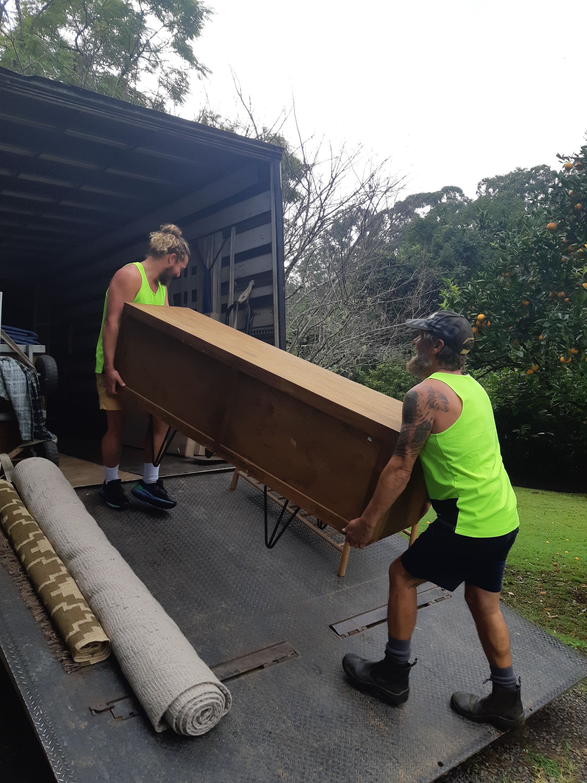 Two Men Are Carrying A Large Box Into The Back Of A Truck — Byron Coast Removals In Main Arm, NSW