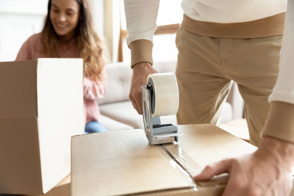 A Man Is Taping A Cardboard Box With Tape — Byron Coast Removals In Main Arm, NSW