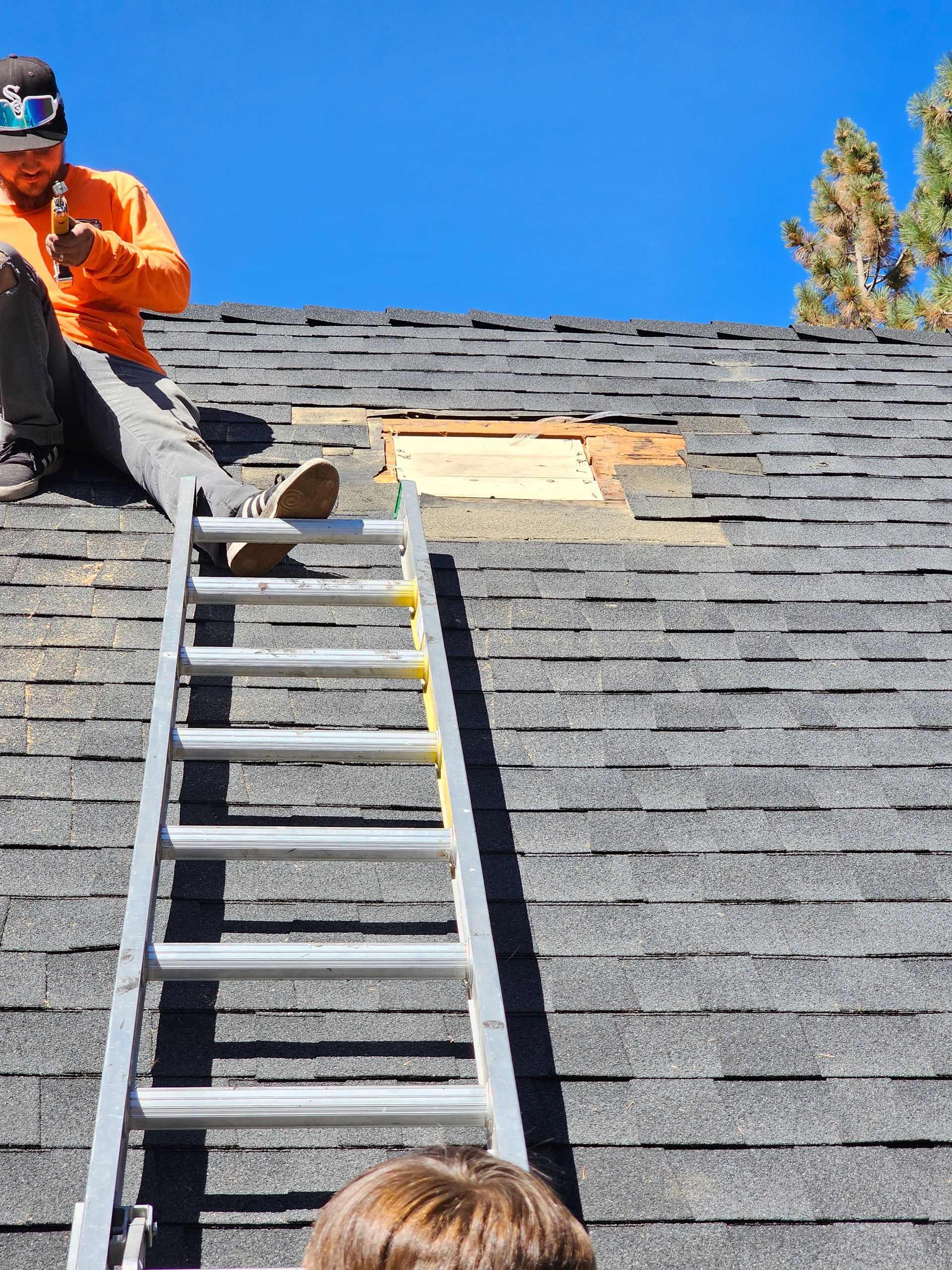 A man is sitting on top of a roof with a ladder.