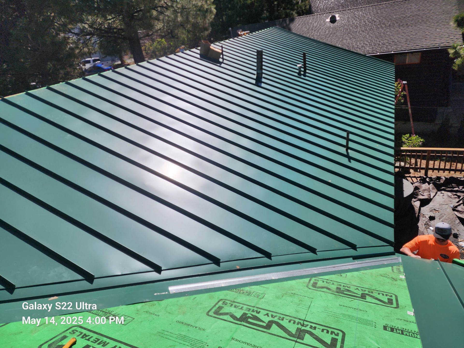 A green metal roof is being installed on a house.