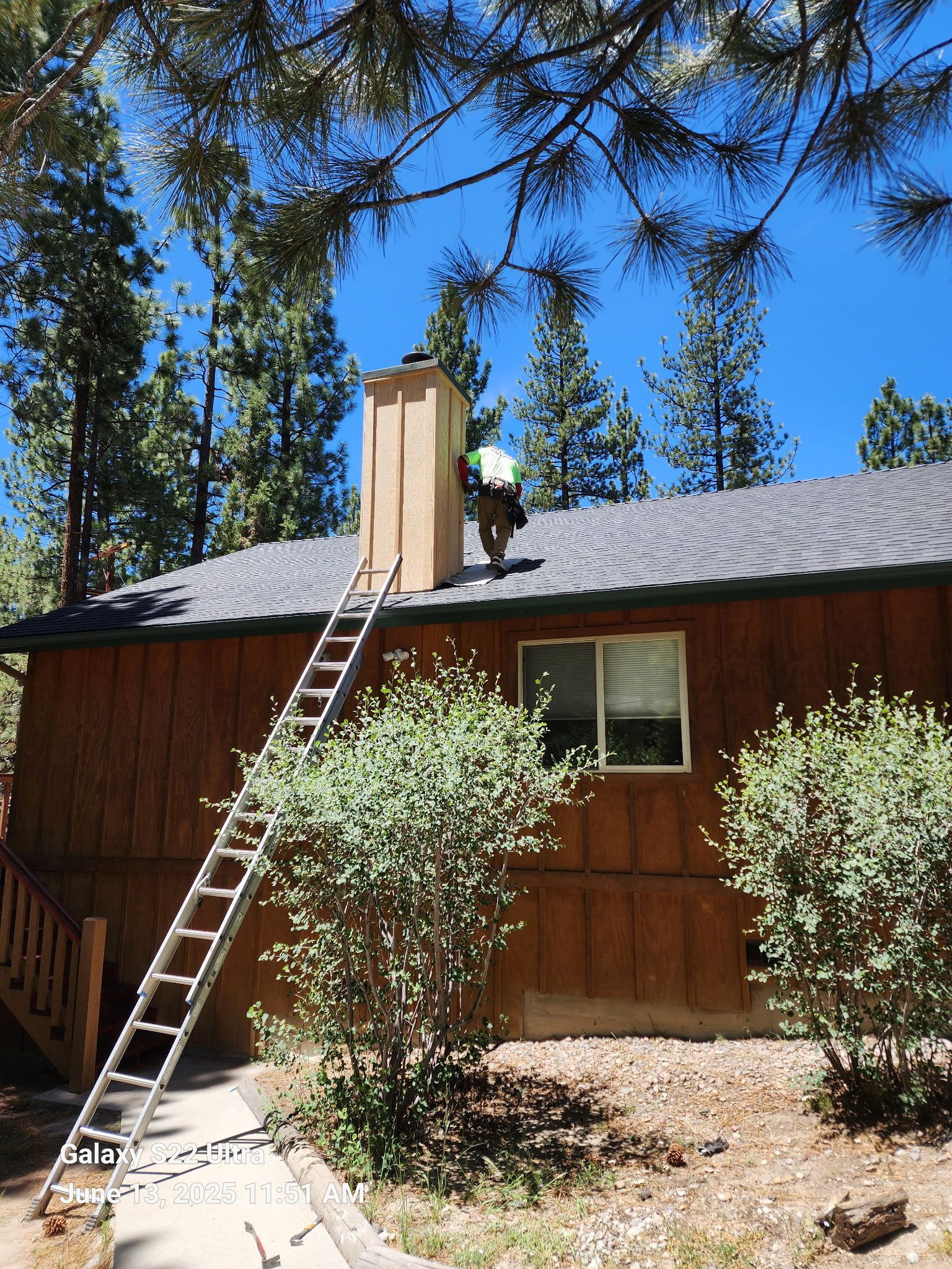A man is working on a chimney on the roof of a house.