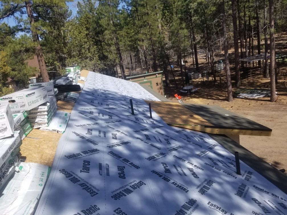 A roof is being built in the woods with trees in the background.