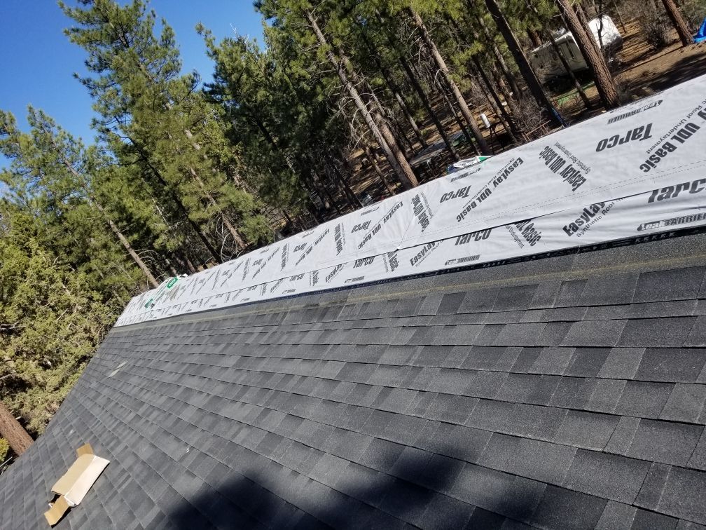 A roof with shingles being installed is surrounded by trees.