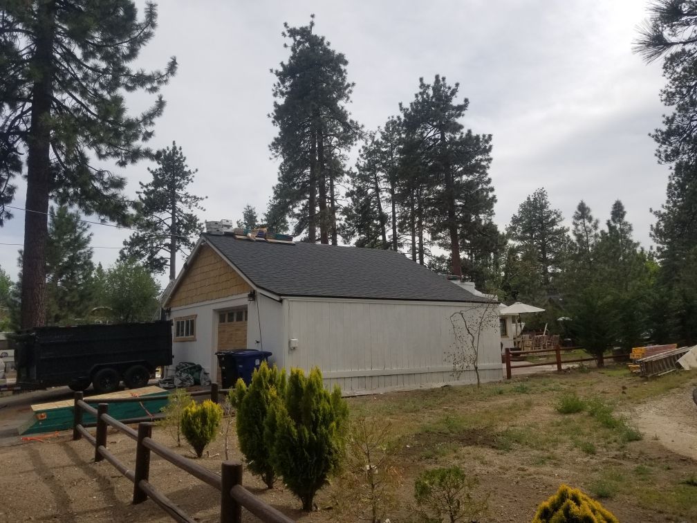 A white house with a black roof is surrounded by trees and a pool.