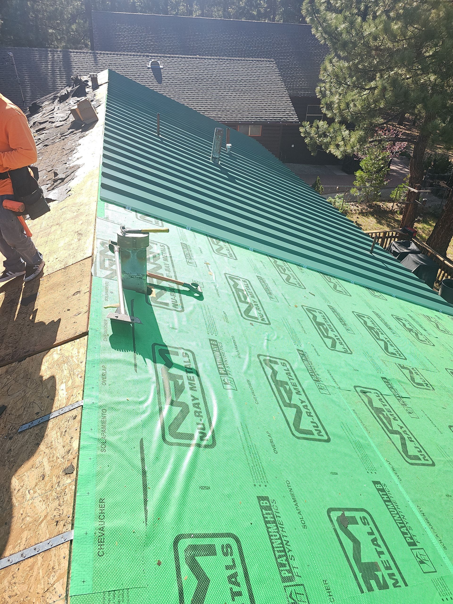 A man is standing on a roof with a green tarp on it.